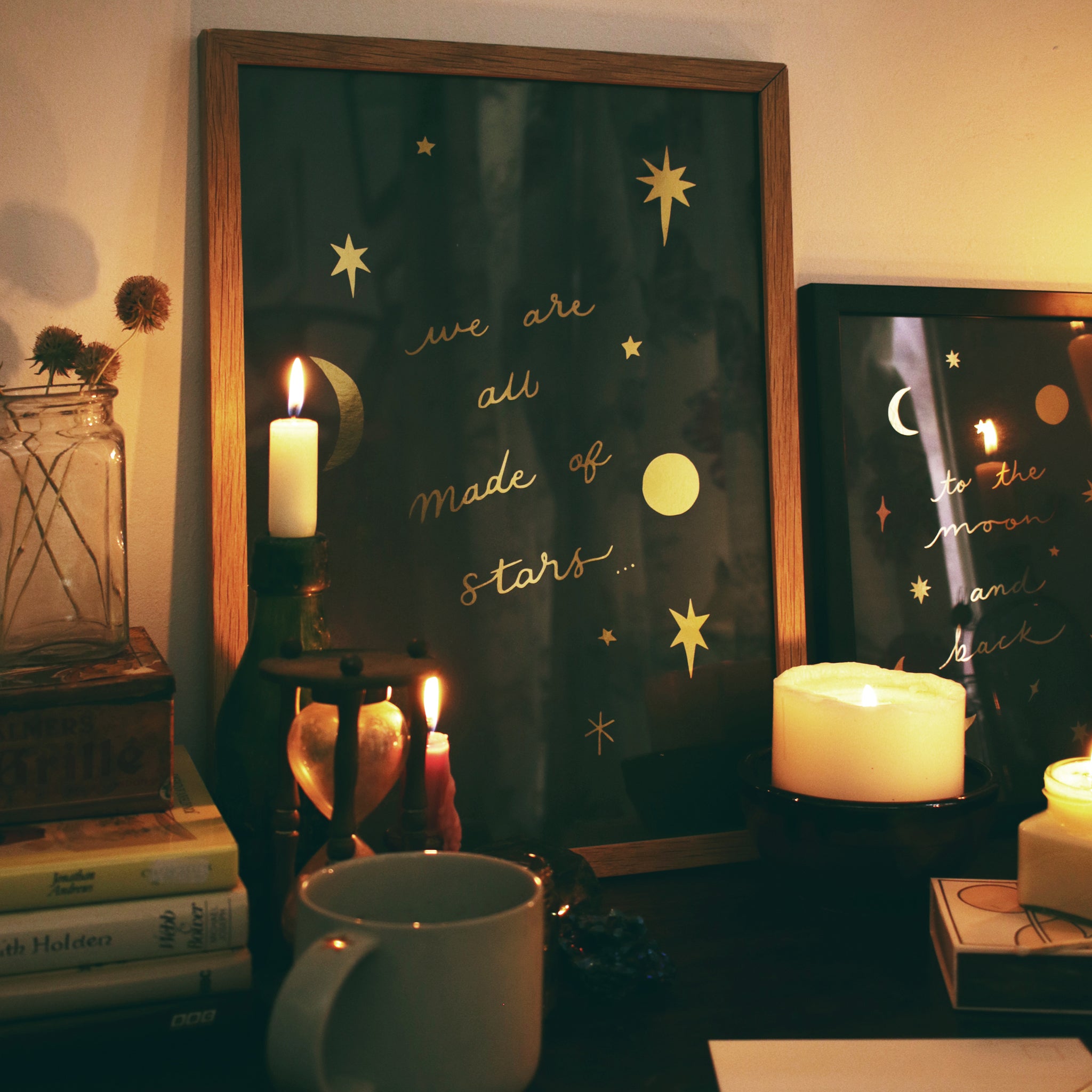 a gold star decorated celestial print in an oak frame sitting on a table surrounded by candles and vintage trinkets