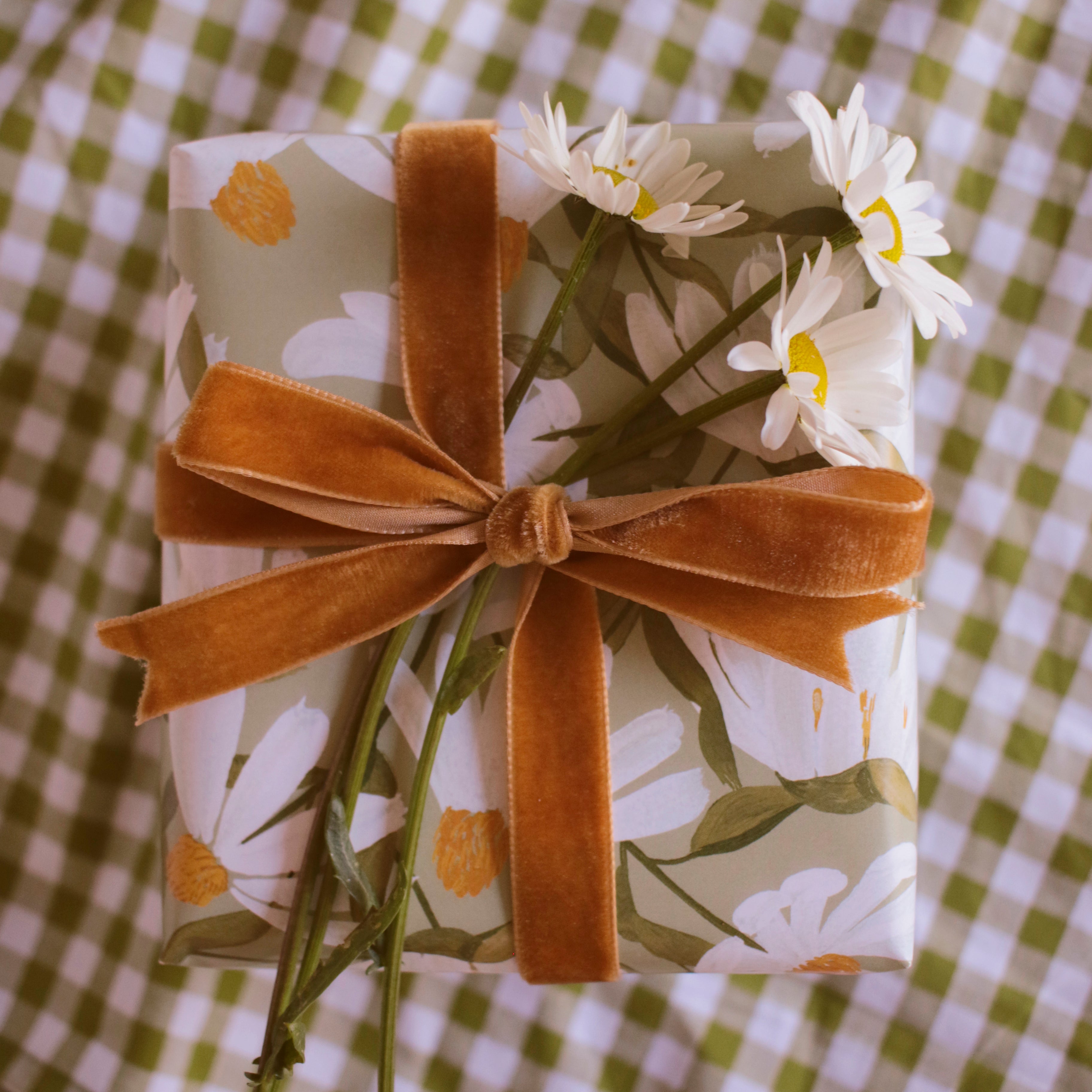 a gift wrapped in green, daisy-patterned wrapping paper, tied with a ochre velvet ribbon