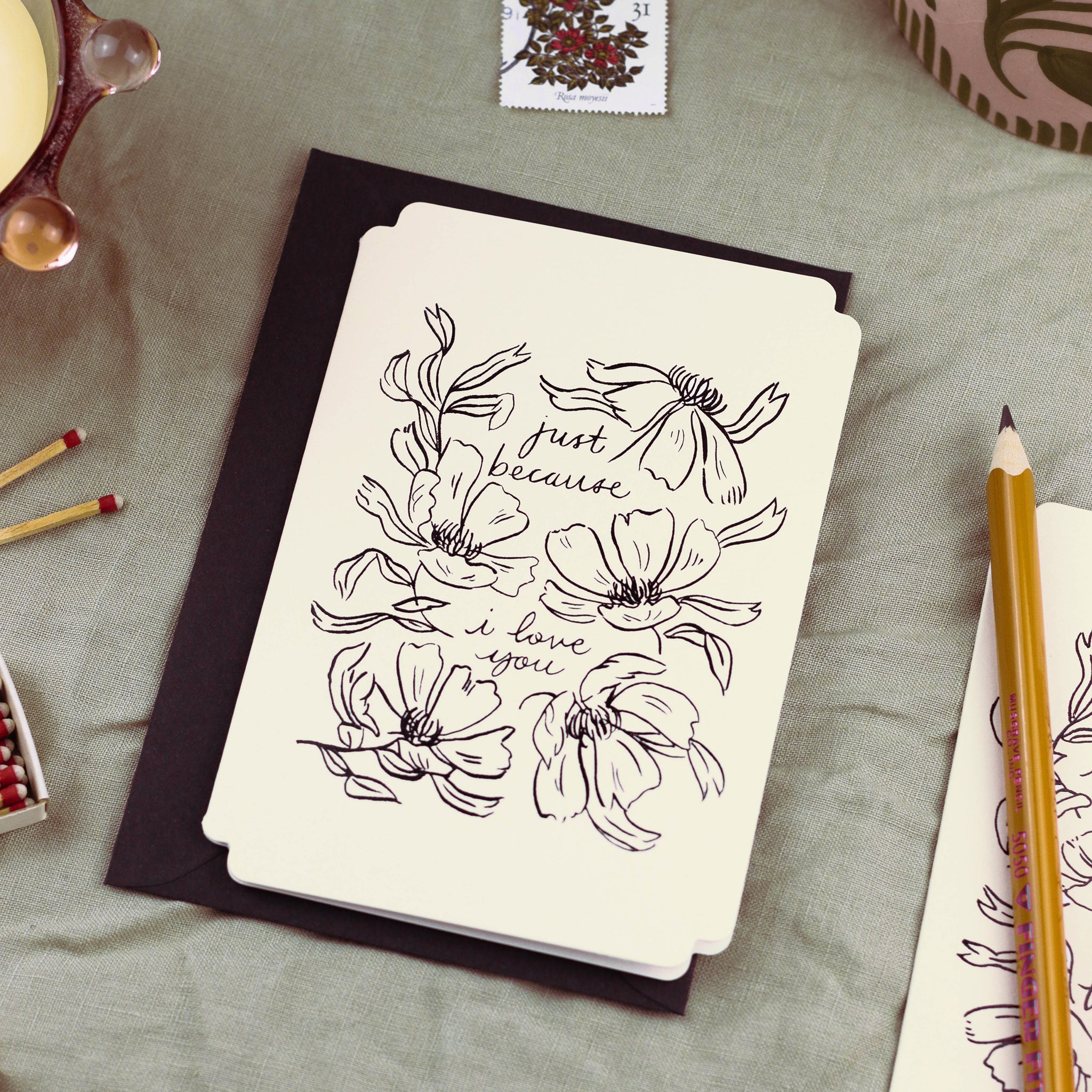 a cream card in a die-cut shape reads "just because I love you" surrounded by linework-style florals. The design is stamped in black foil. - Annie Dornan Smith
