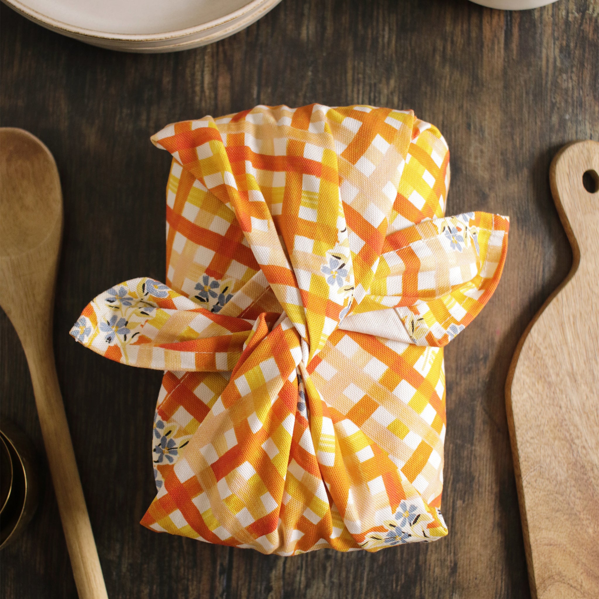 A gingham and floral patterned tea towel, bundled around a lunchbox furoshiki-style