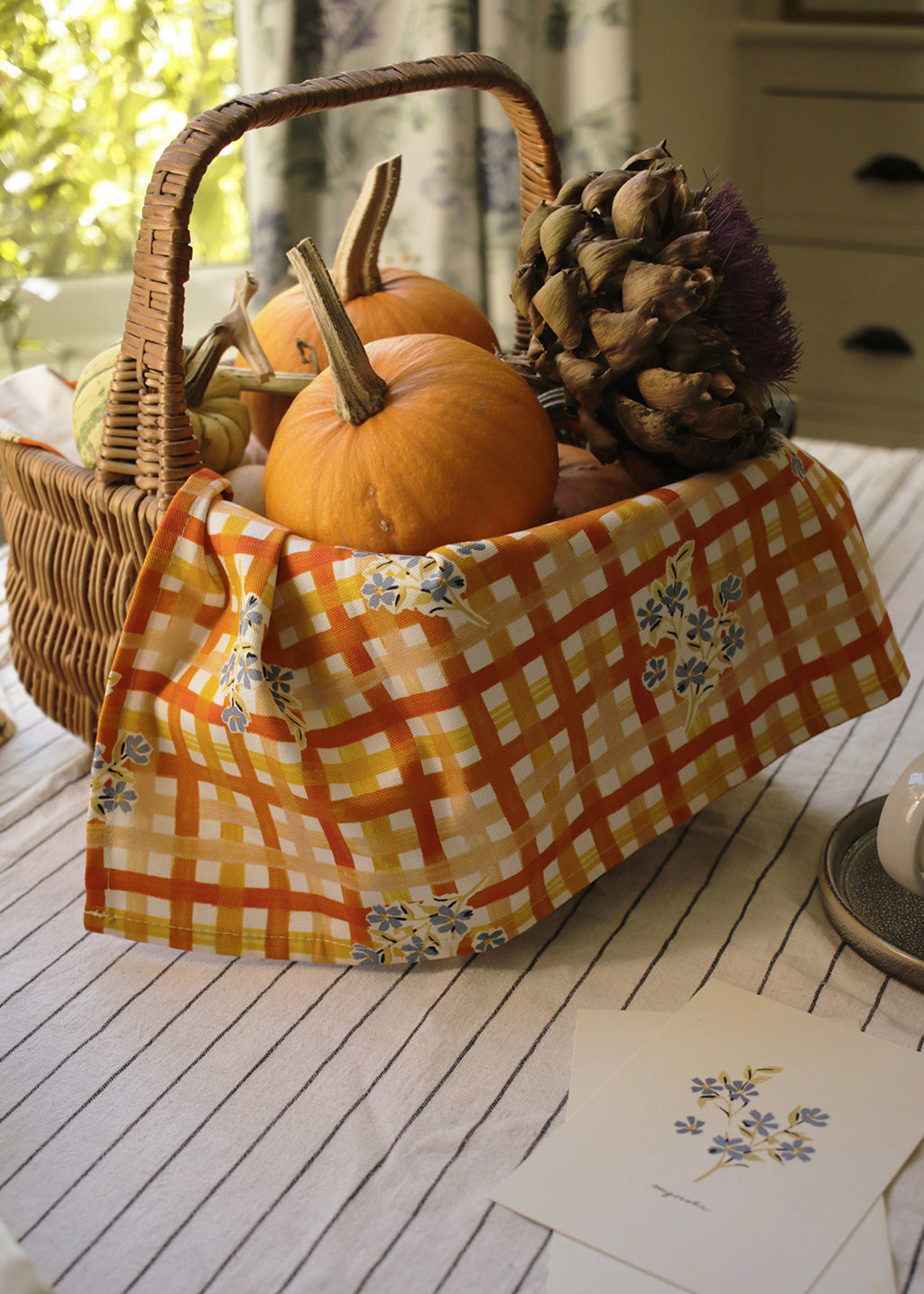 the gingham and floral patterned teatowel used to decorate a gift basket of pumpkins and dried flowers