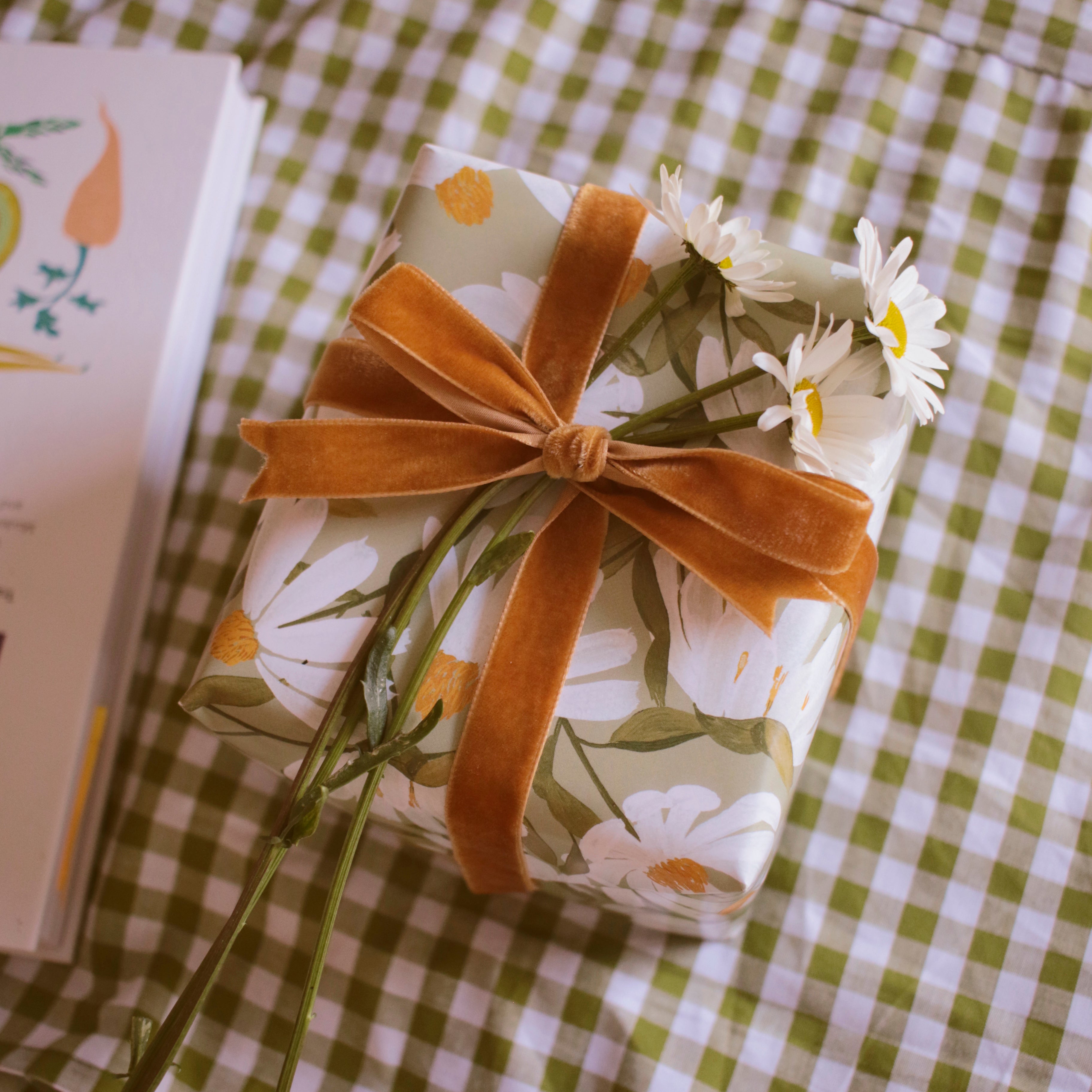 a gift wrapped in floral paper with a velvet bow, and finished with fresh daisy flowers