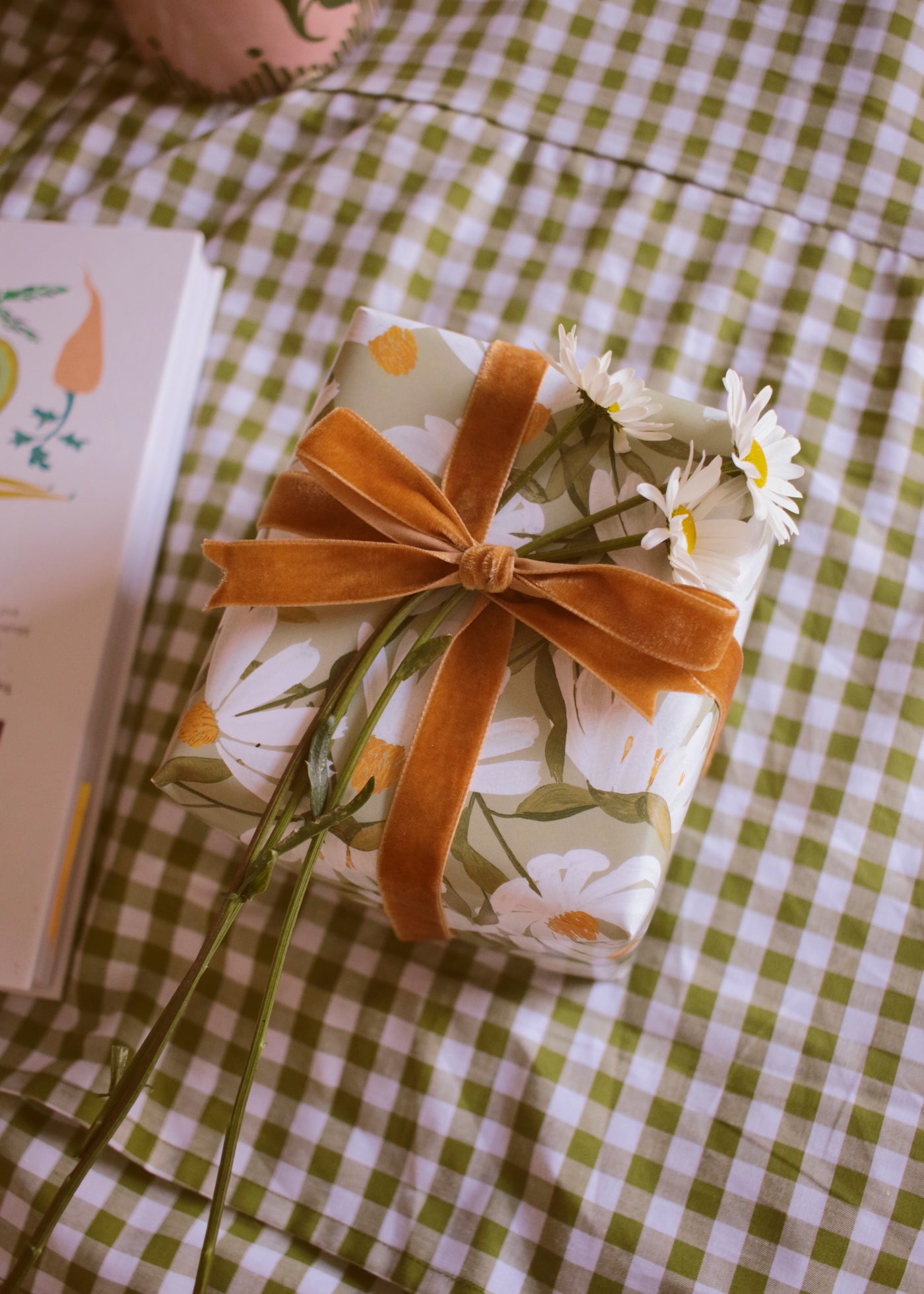 a gift wrapped in floral paper with a velvet bow, and finished with fresh daisy flowers