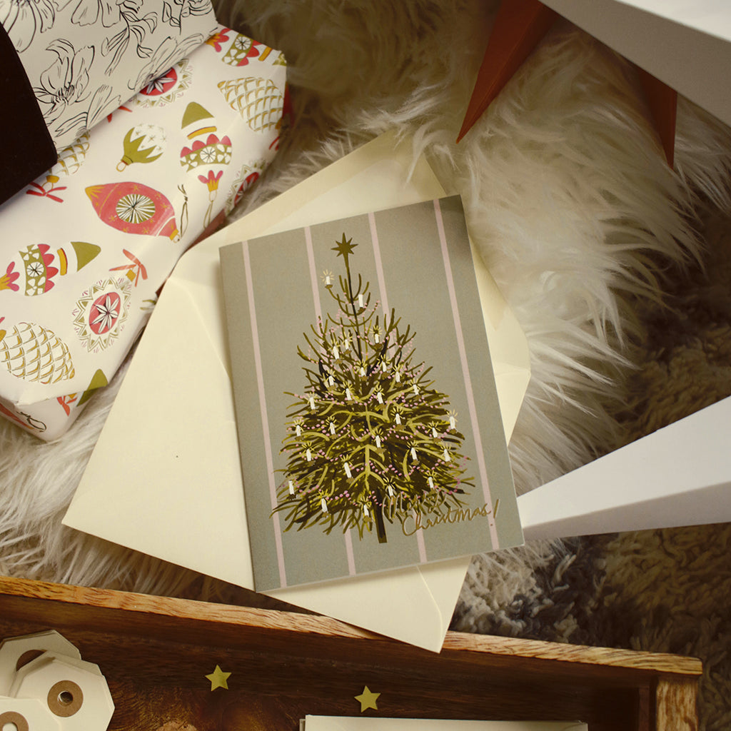 an illustrated Christmas tree card with cream envelope, nestled amongst the gifts and decorations