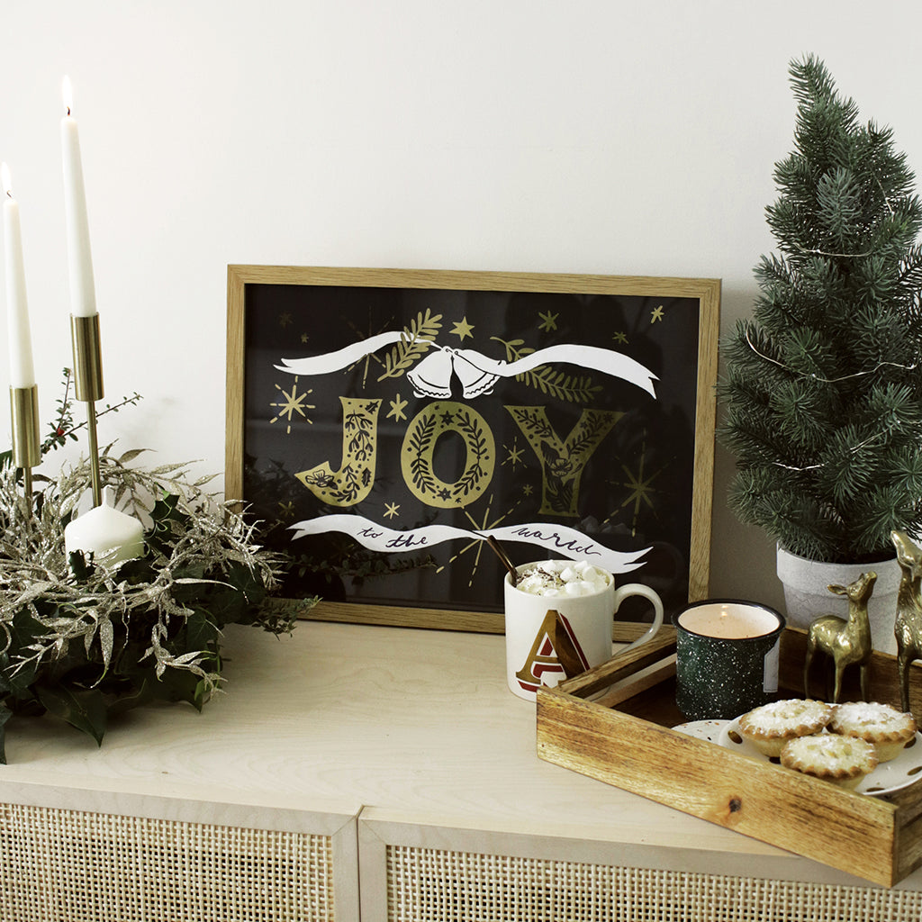 Navy Christmas Print With Gold Joy Lettering And Stars In An Oak Frame With Mug Of A Hot Chocolate - Annie Dornan Smith
