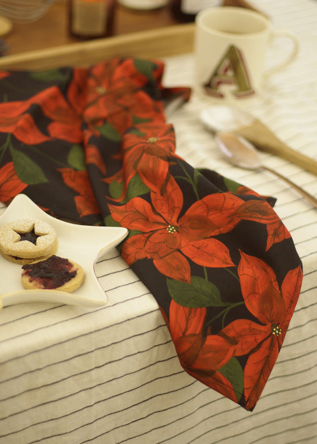 A cotton teatowel with a black and red poinsettia patterned print, on a christmassy table