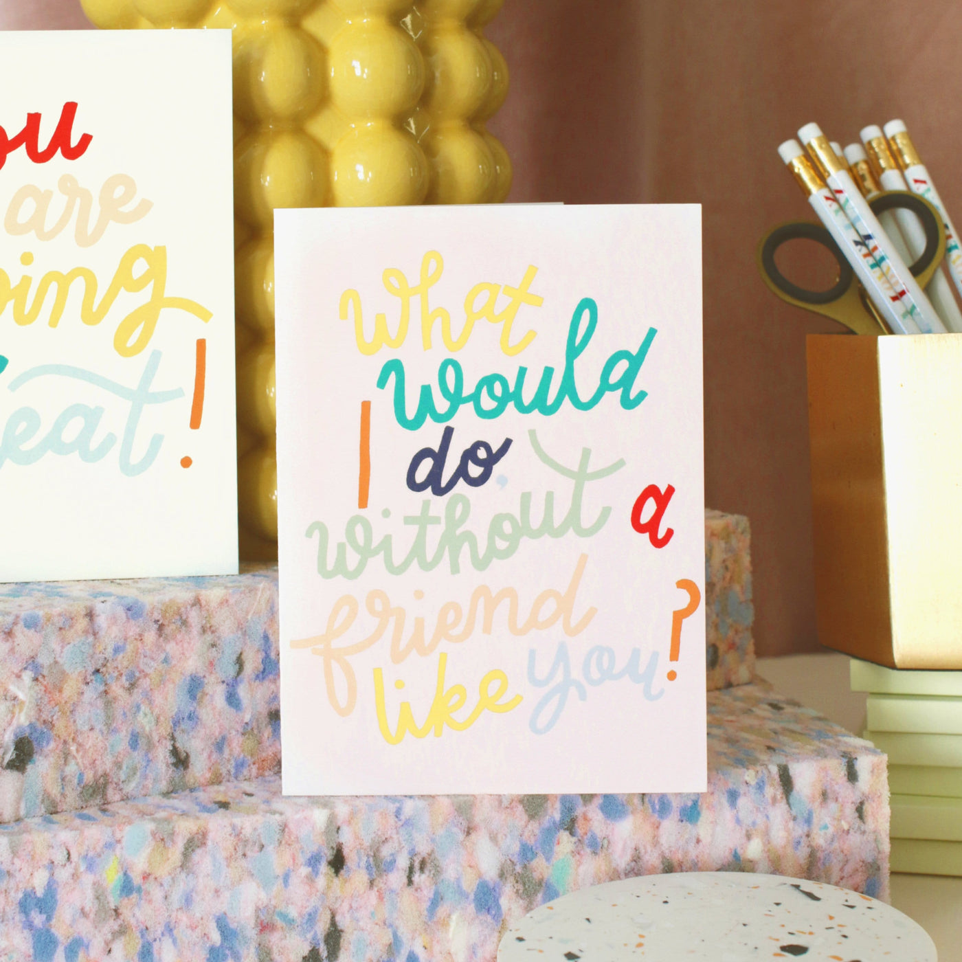 A Hand Lettered Rainbow Typography Card Which Reads What Would I Do Without A Friend Like You On A Desk - Annie Dornan Smith