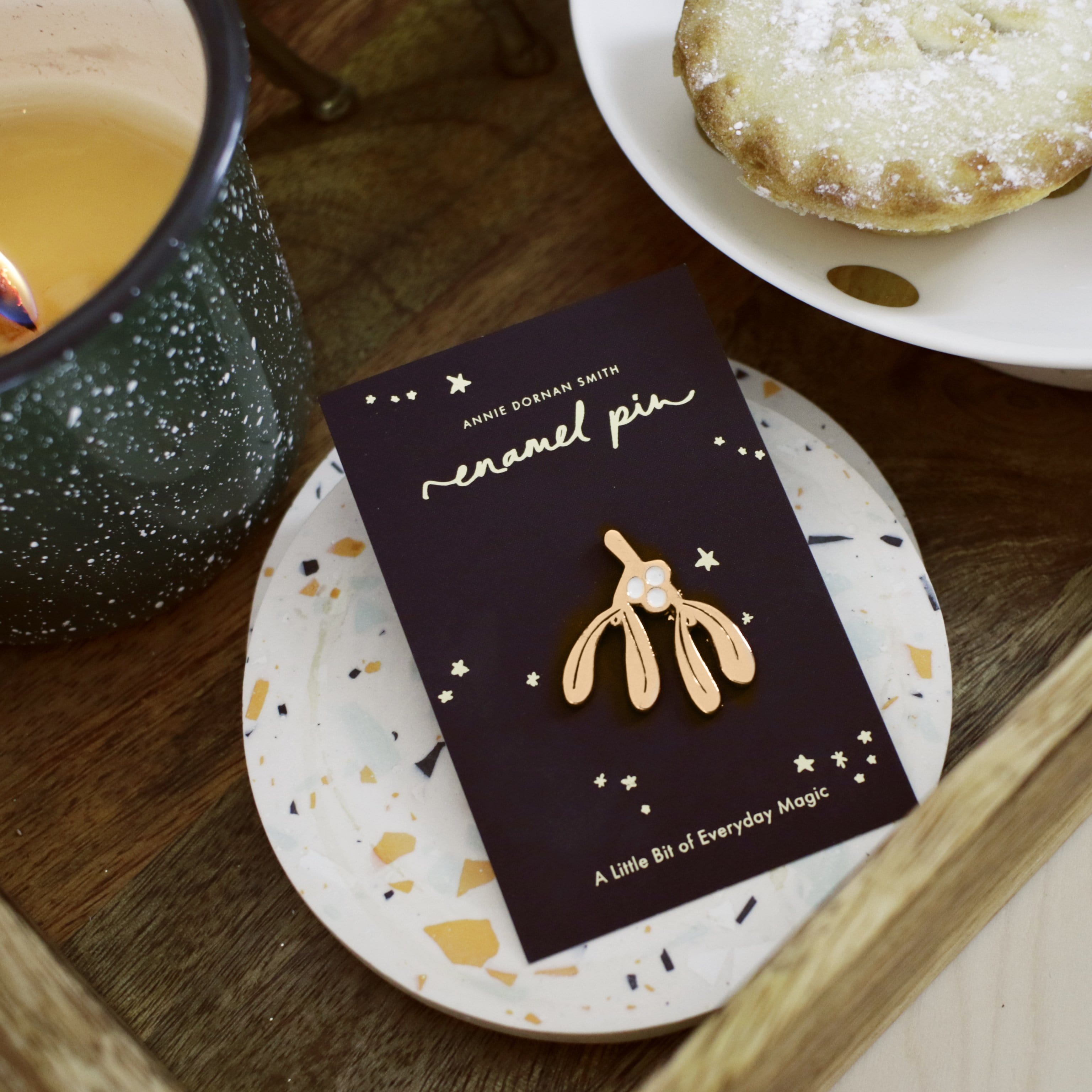 Rose Gold Enamel Mistletoe Shaped Pin On A Black Backing Board Next To A Mice Pie - Annie Dornan Smith