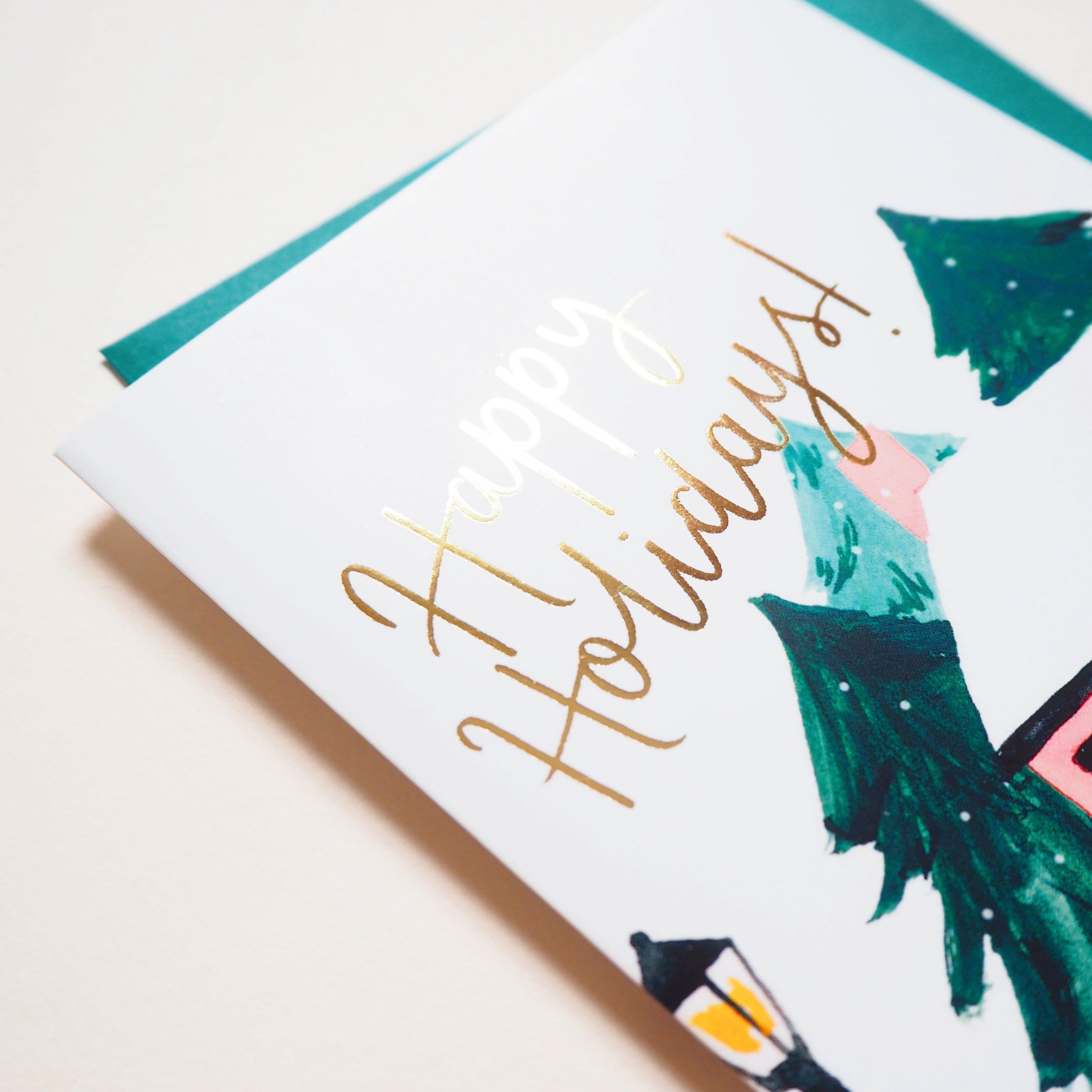 Close Up Of An Illustrated Snowy Cottage Christmas Card With Merry Christmas In Gold With A Teal Envelope - Annie Dornan Smith