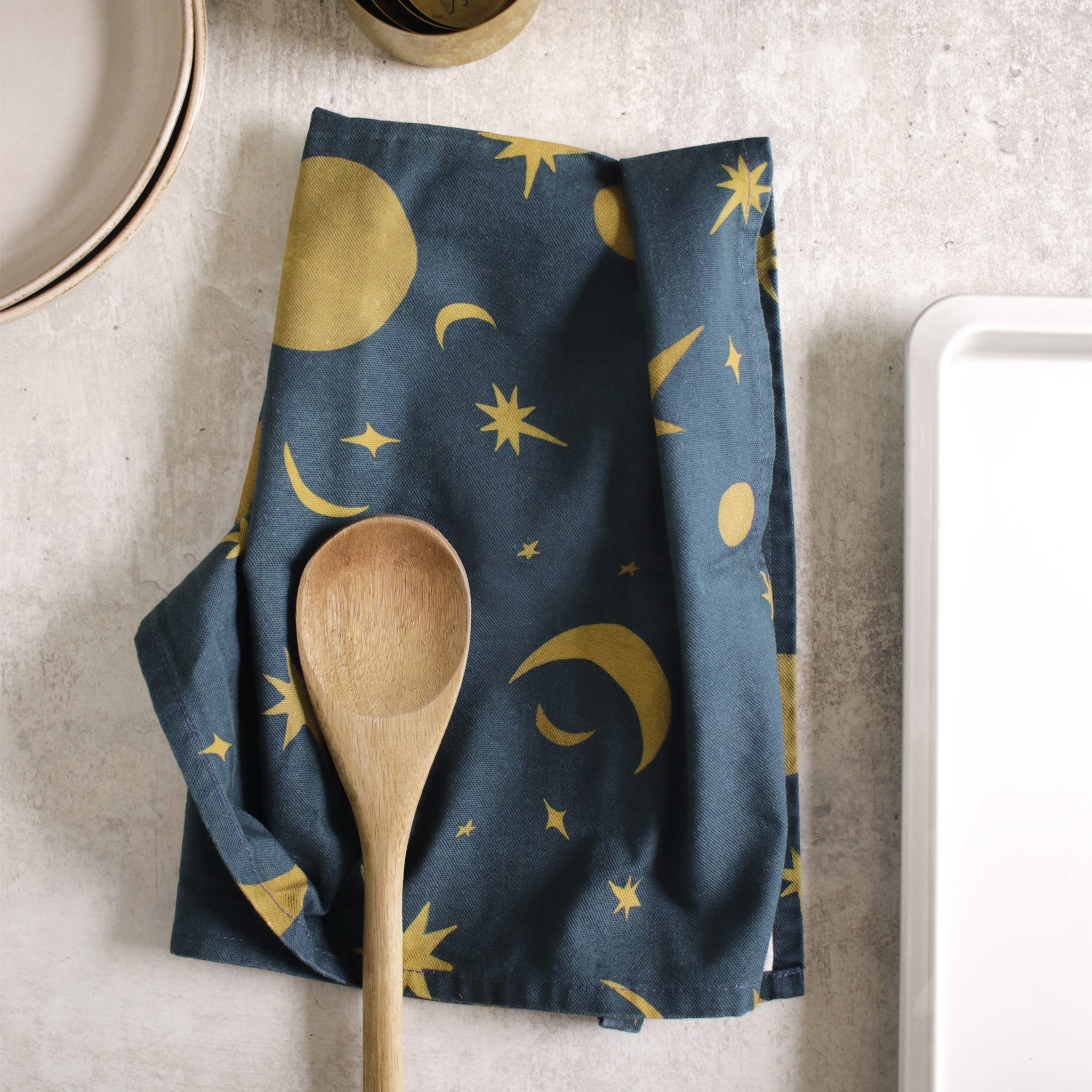 A navy and gold celestial pattern tea towel on a concrete countertop