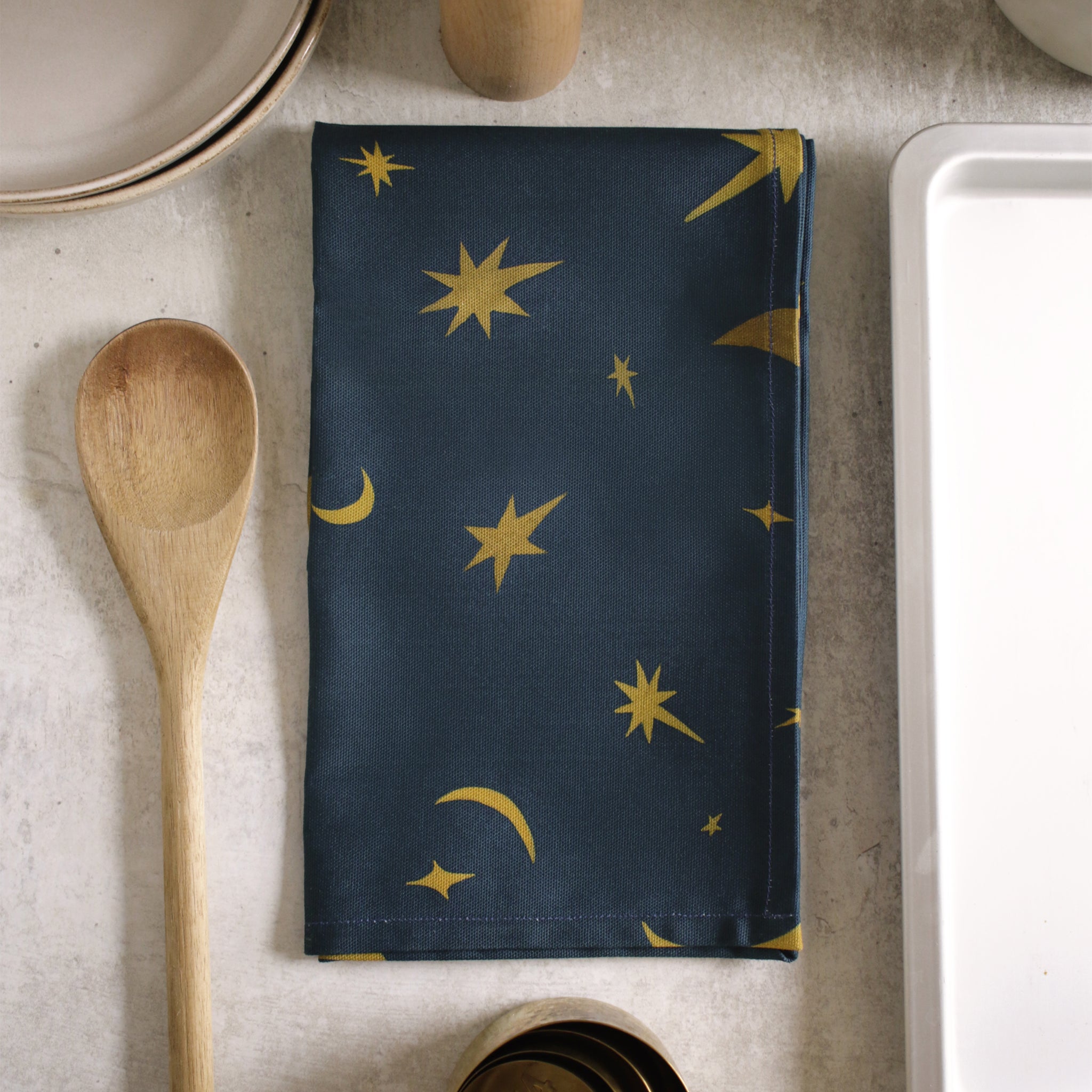 a space-pattern cotton tea towel on a wooden table top, alongside baking ingredients