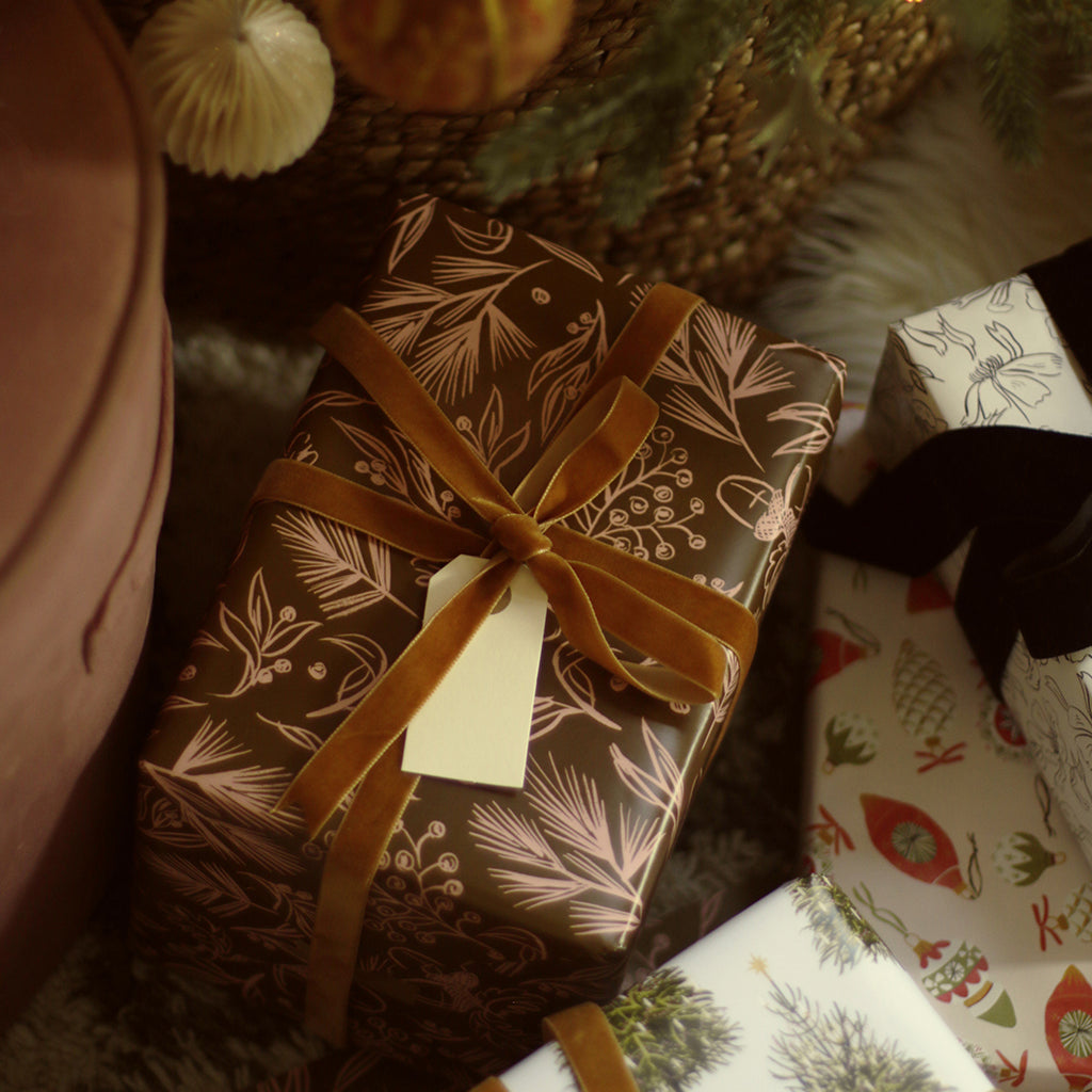a gift wrapped in brown foliage patterned wrapping paper sits under the tree