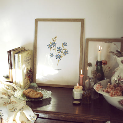 myosotis print in oak frame on a cottage style table with candles and books