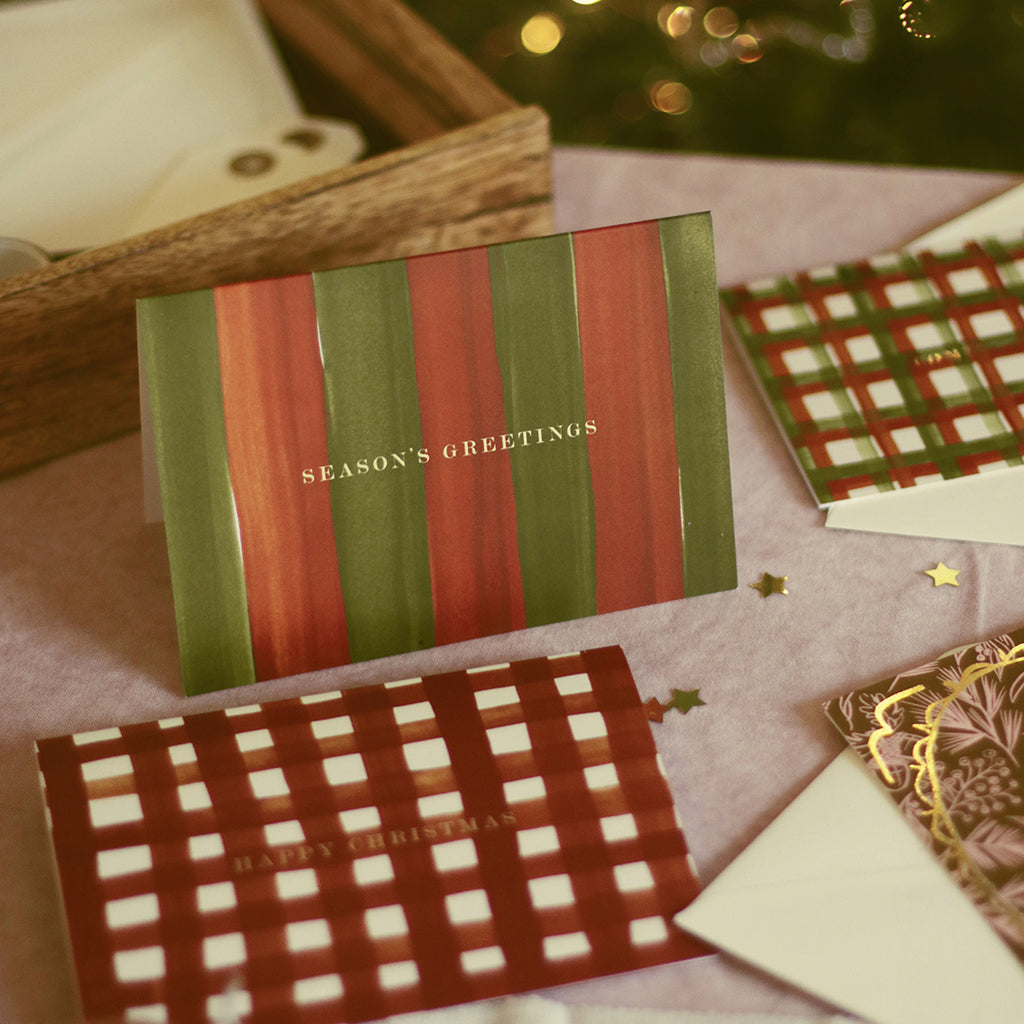 a red and green striped christmas card walongside other festive greetings on a pink tableclotth