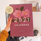 holding last year's 2021 calendar in my studio. A label on the image says "updated for 2022!".