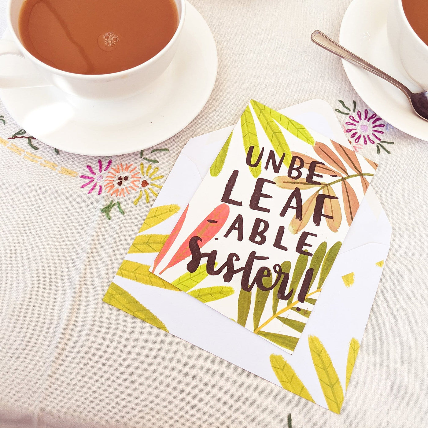 An Illustrated Leaf Greeting Card With The Words Unbeleafable Mum With A Matching Leaf Envelope Next To A Cup Of Tea - Annie Dornan Smith