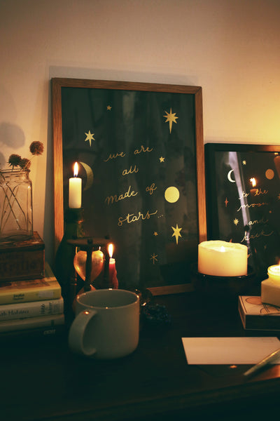 a gold star decorated celestial print in an oak frame sitting on a table surrounded by candles and vintage trinkets