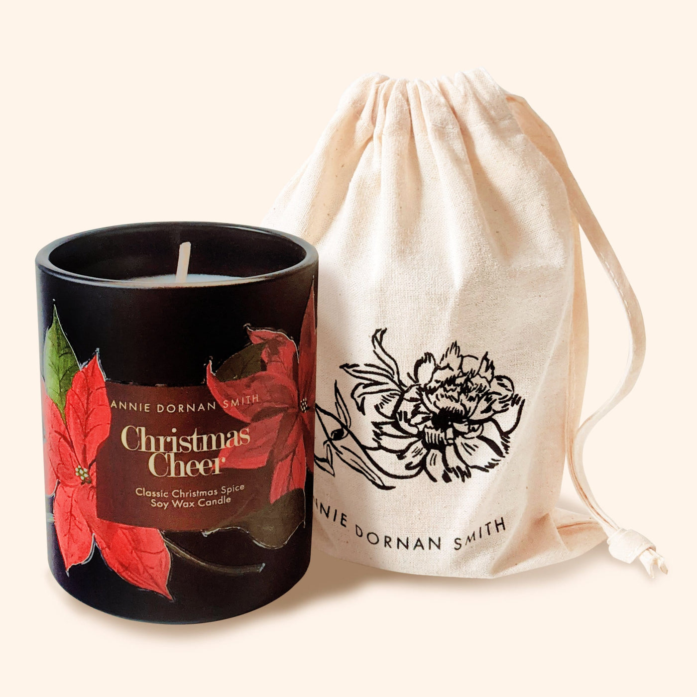 A Black Glass Candle Decorated with Red Poinsettias And A Christmas Cheer Label Alongside Linen Draw String Bag - Annie Dornan Smith