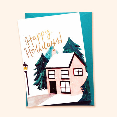 An Illustrated Snowy Cottage Christmas Card With Merry Christmas In Gold With A Teal Envelope - Annie Dornan Smith