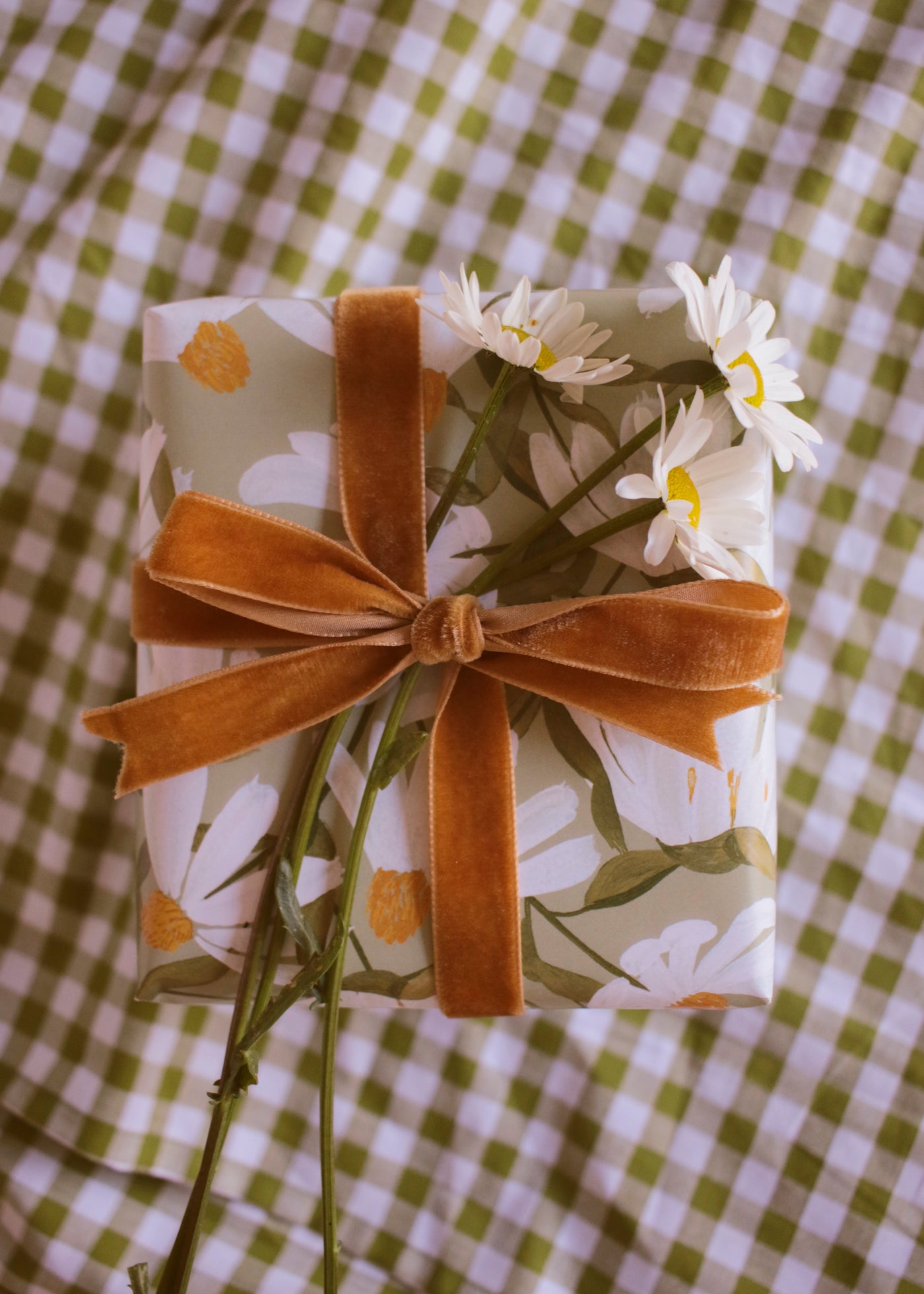 a gift wrapped in green, daisy-patterned wrapping paper, tied with a ochre velvet ribbon