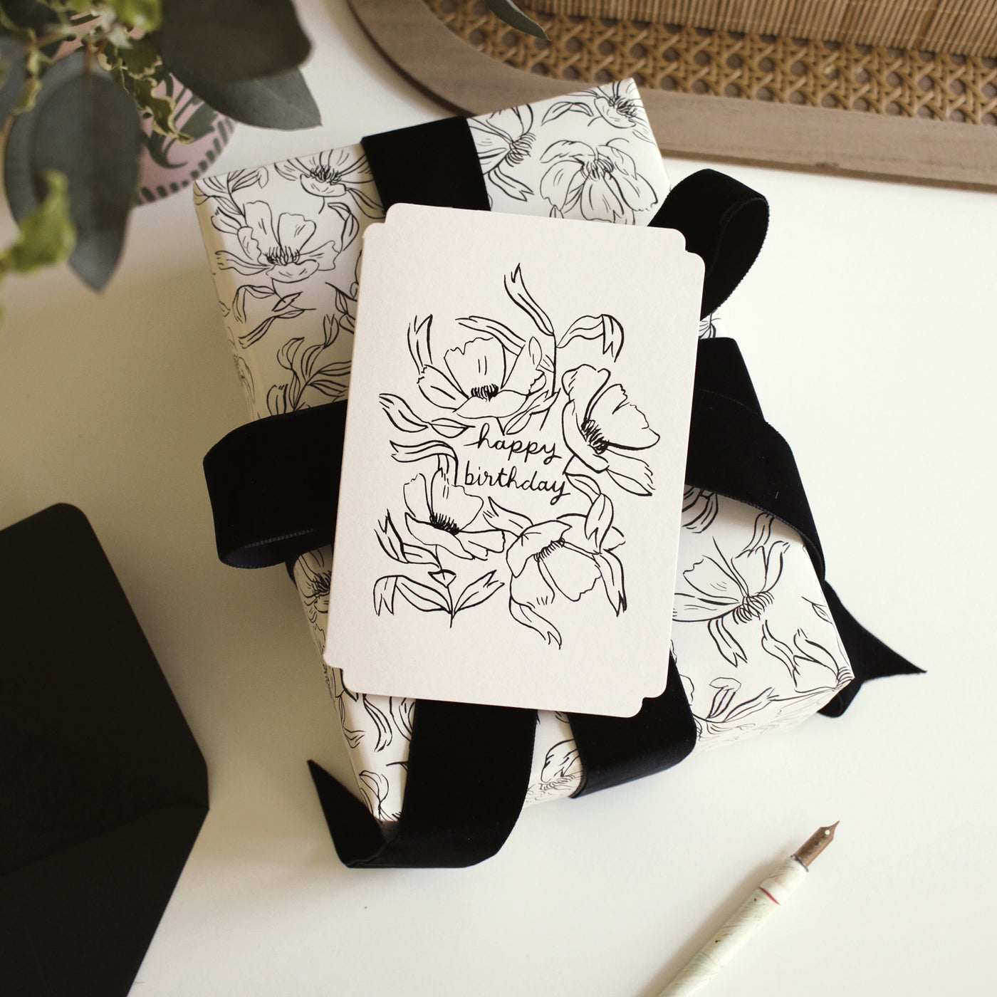 An illustrated floral birthday card sits atop a gift wrapped in matching, linework-style floral illustrations.  - Annie Dornan Smith
