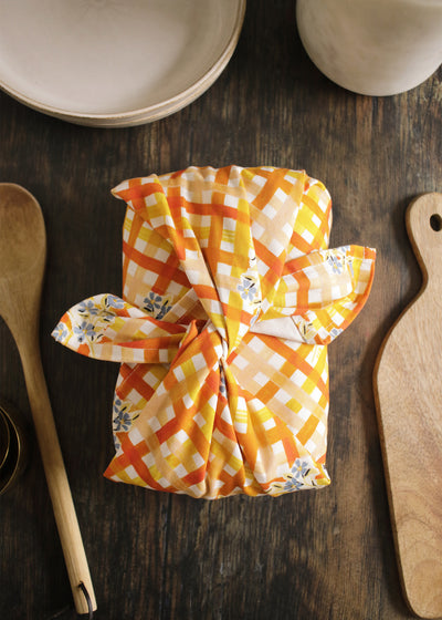 A gingham and floral patterned tea towel, bundled around a lunchbox furoshiki-style