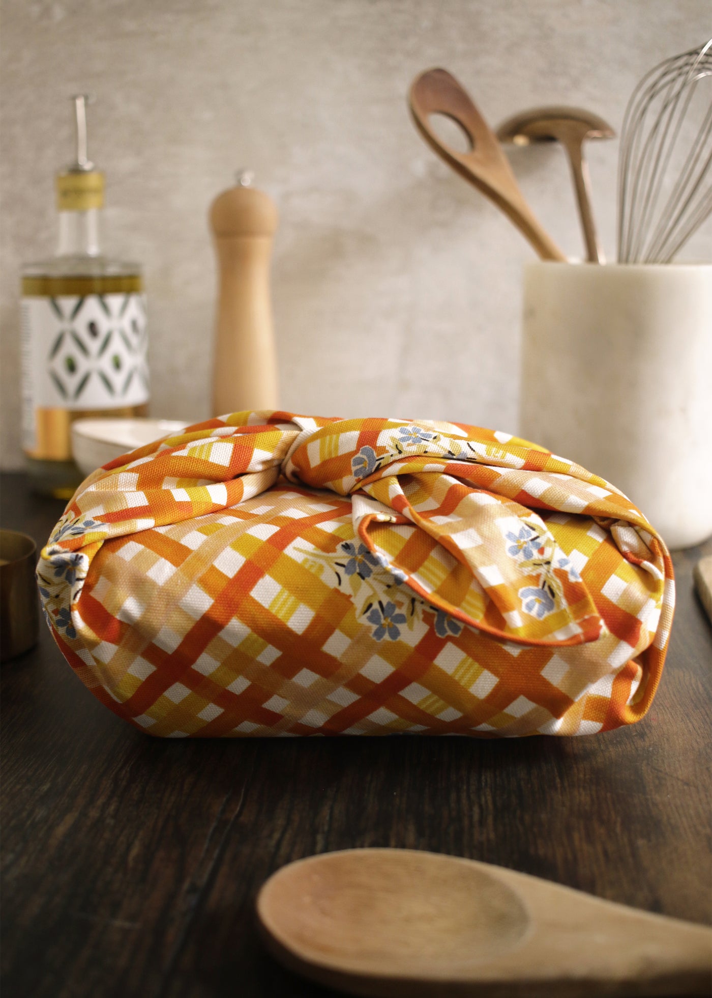 A gingham and floral patterned tea towel, bundled around a lunchbox furoshiki-style