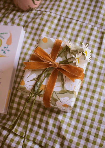 a gift wrapped in floral paper with a velvet bow, and finished with fresh daisy flowers