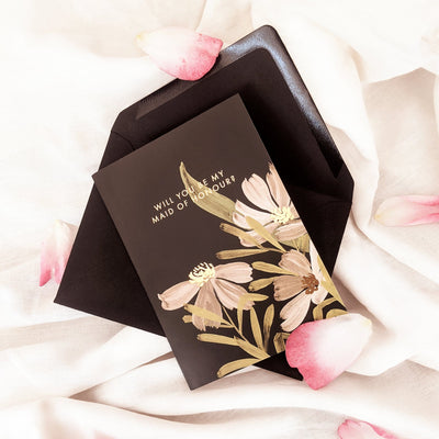 A Floral A6 Card With White And Green Flowers With Will You Be My Maid Of Honour In Gold Lettering  With Black Envelope With Petals - Annie Dornan Smith
