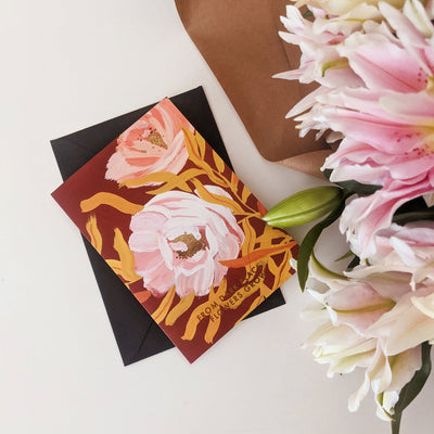 Botanical Greeting Card Pink English Tea Roses On Warm Brown Background With The Words From Dark Places Flowers Grow In Gold With Black Envelope Next To A Bunch Of Lilys - Annie Dornan Smith