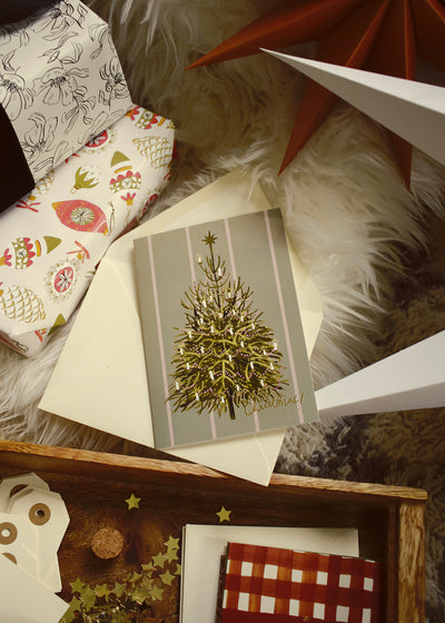 an illustrated Christmas tree card with cream envelope, nestled amongst the gifts and decorations