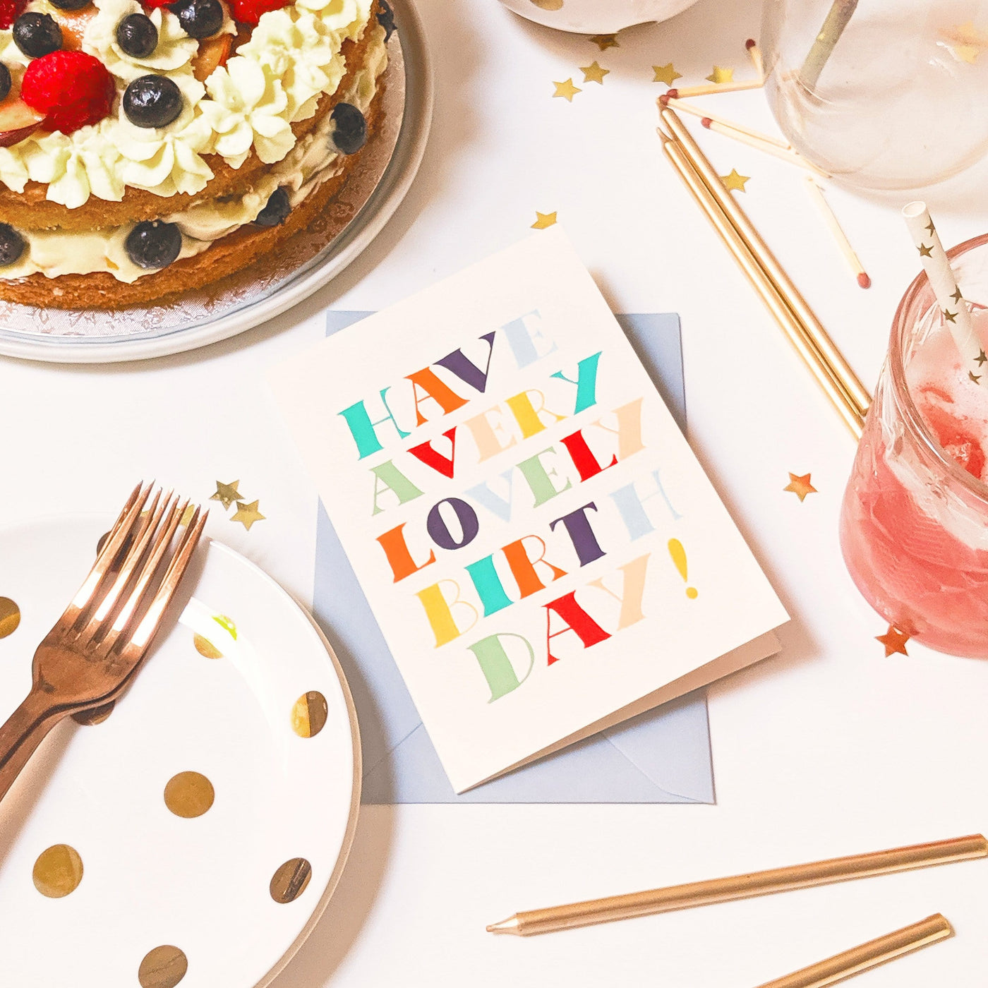 A Hand Lettered Rainbow Typography Card Reading Have A Very Lovely Birthday With A Pale Grey Envelope On A Party Table - Annie Dornan Smith