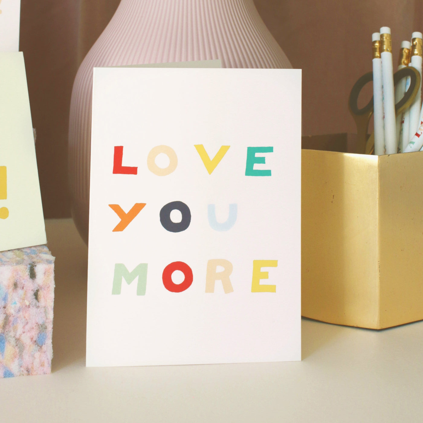 A Hand Lettered Rainbow Typography Card Reading Love You More Next To A Yellow Pencil Pot  - Annie Dornan Smith
