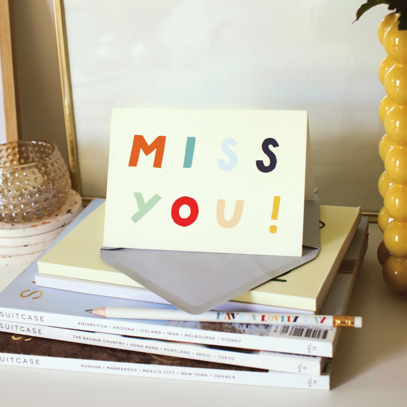 A Hand Lettered Rainbow Typography Card Which Reads Miss You With Pale Grey Envelope On A Pile Of Books - Annie Dornan Smith