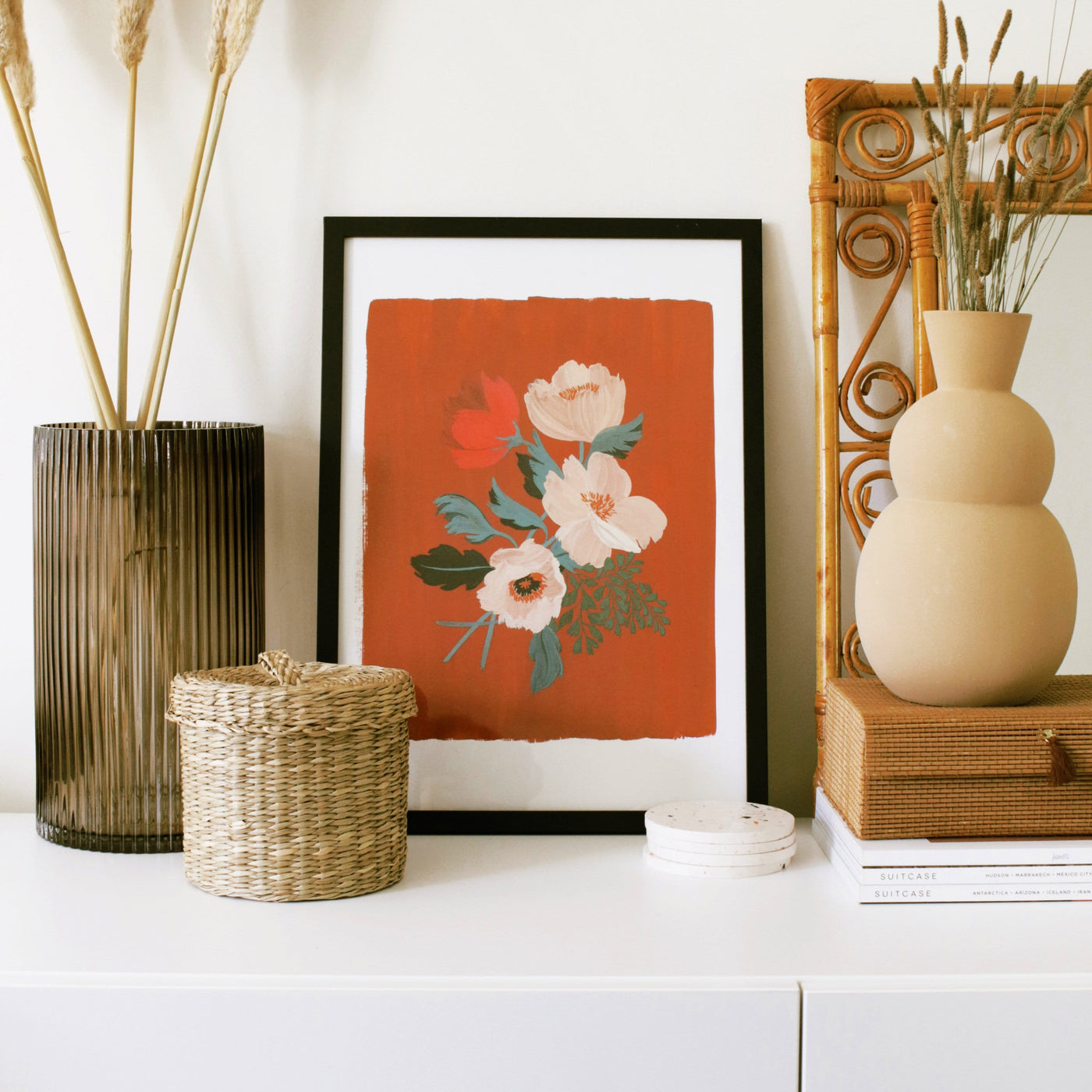 Red Floral Botanical Art Print With A Spray of Anemone Flowers On A Deep Red Background In A Black Frame Next To A Tall Vase And Rattan Pot - Annie Dornan Smith