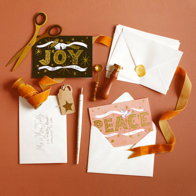 Coral Christmas Card With Gold Peace Lettering And Stars With A White Ribbon And Dove On An Orange Background Orange Velvet Ribbon And Wrapping Accesorries - Annie Dornan Smith