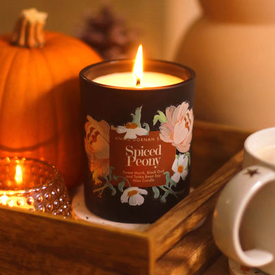 A Black Candle with Spiced Peony Label  with Floral illustrations Burning - Annie Dornan Smith
