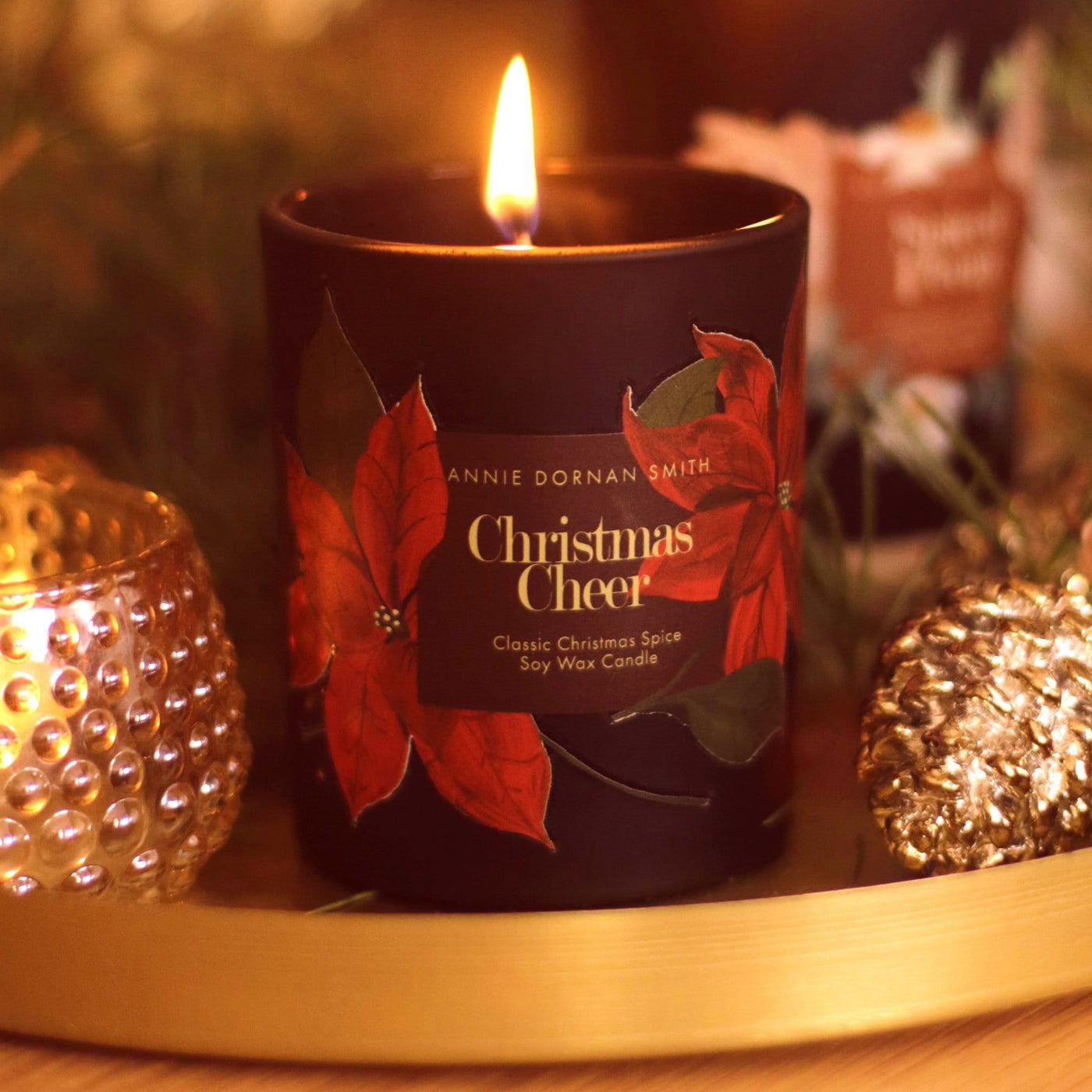 A Black Glass Candle Decorated with Red Poinsettias And A Christmas Cheer Label - Annie Dornan Smith