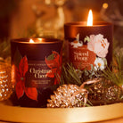 A Black Glass Candle Decorated with Red Poinsettias And A Christmas Cheer Label On A Gold Tray With Christmas Decorations  - Annie Dornan Smith