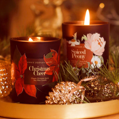 Two Black Candles with Spiced Peony And Christmas Cheer Labels  with Floral illustrations Burning - Annie Dornan Smith