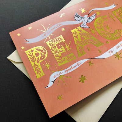 Coral Christmas Card With Gold Peace Lettering And Stars With A White Ribbon And Dove With A Gold Envelope - Annie Dornan Smith