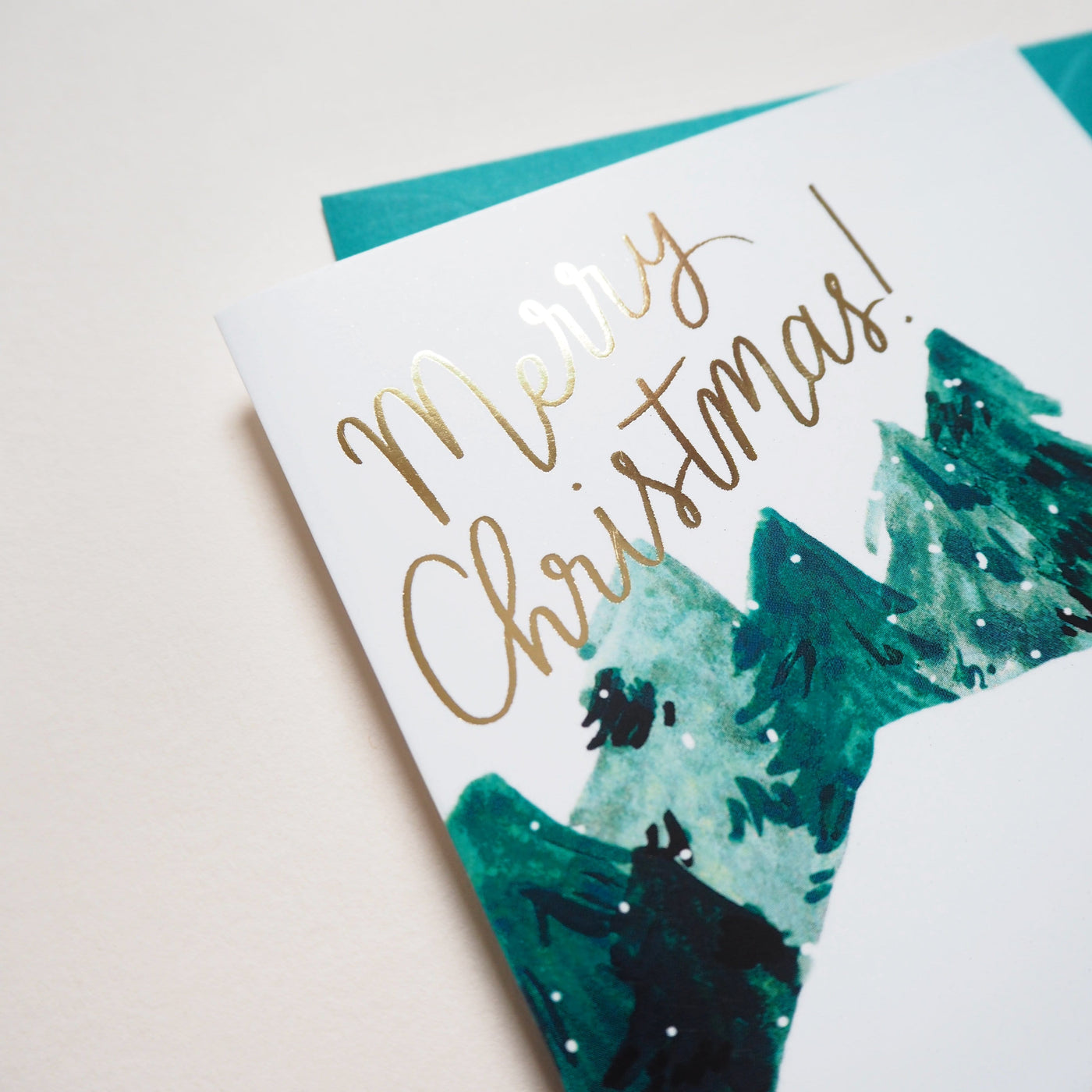 Close Up Of An Illustrated Snowy Chalet Christmas Card With Merry Christmas In Gold With A Teal Envelope - Annie Dornan Smith