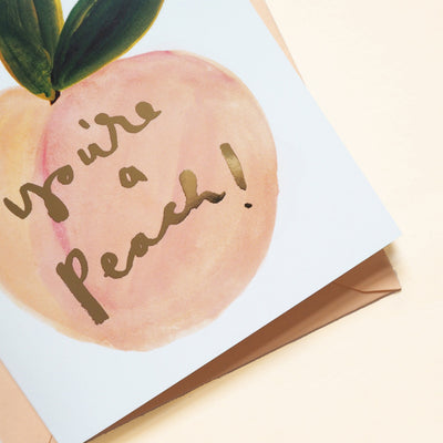 An Illustrated Care With A Peach And Green Leaf With The Words You're A Peach In Gold With A Peach Envelope - Annie Dornan Smith