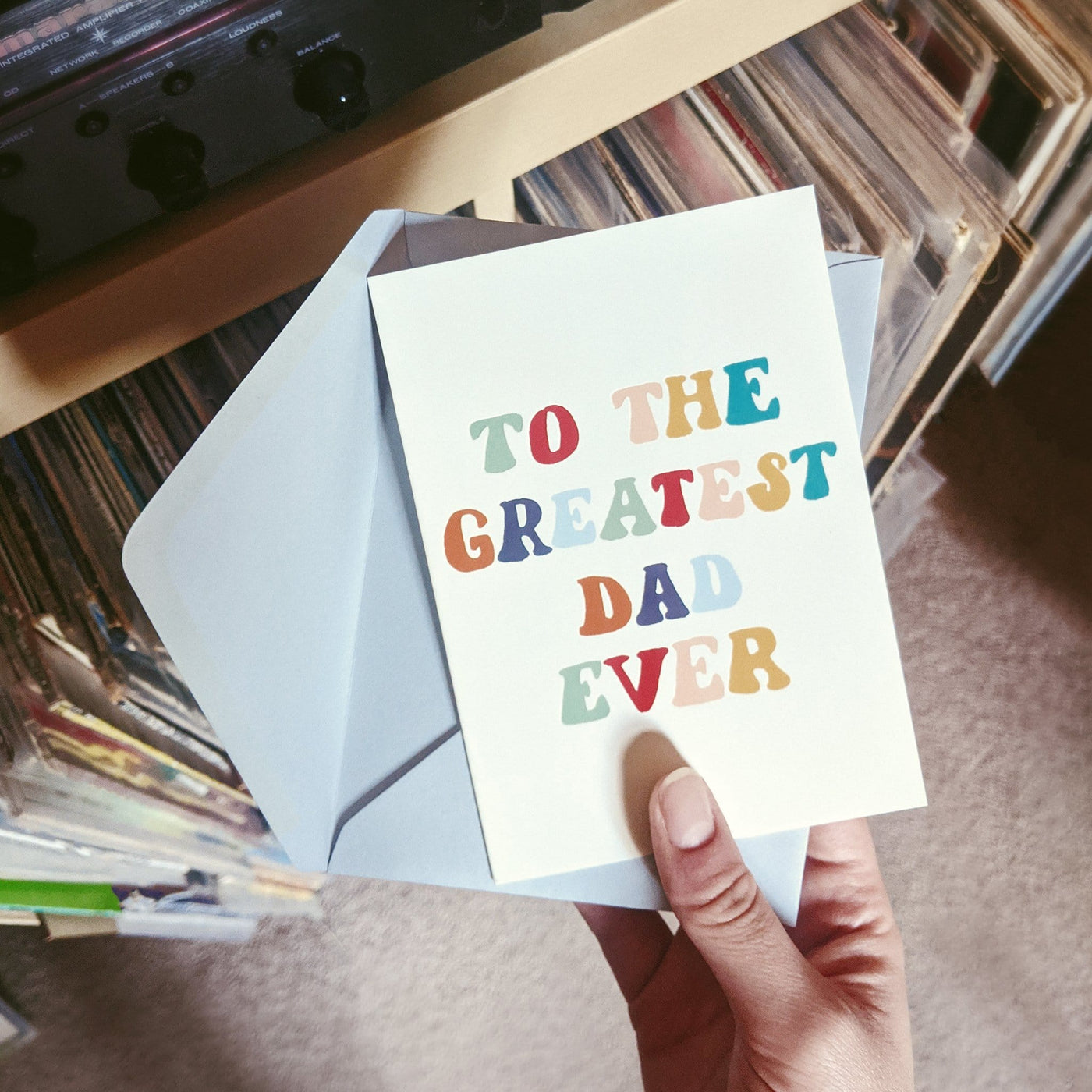 A Hand Lettered Rainbow Typography Father's Day Card Which Reads To the Greatest Dad Ever With Pale Grey Envelope In Front Of A Stack Of Records - Annie Dornan Smith