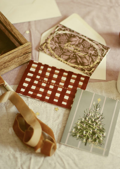 a red checkered christmas card alongside other christmas greetings, laid out on a pink tablecloth