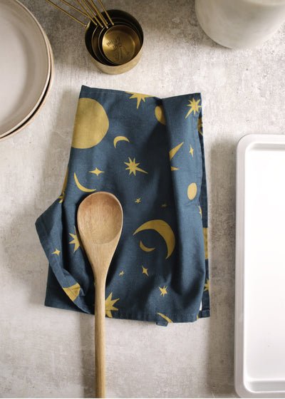 A navy and gold celestial pattern tea towel on a concrete countertop