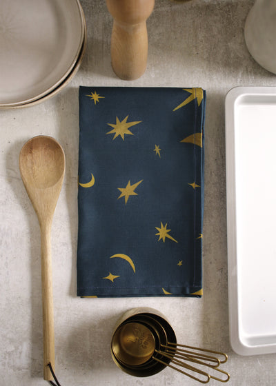 a space-pattern cotton tea towel on a wooden table top, alongside baking ingredients