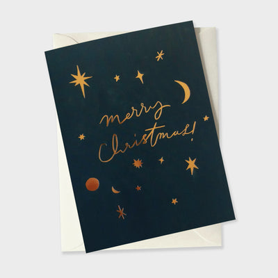 a celestial greetings card with a navy paint-textured background, covered in gold foil moons and stars reads "merry crhristmas!"