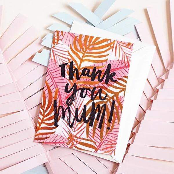 An Illustrated Pink Palm Leaf Card With The Words Thank You Mum In Brush Lettering With A White Envelope On A Pile Of Paper Leaves - Annie Dornan Smith