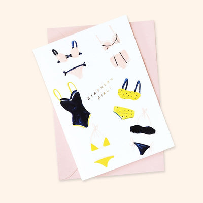 An illustrated Birthday Card With Pink yellow And Black Bikinis On And Birthday Girl In Gold With A Pale Pink Envelope - Annie Dornan Smith